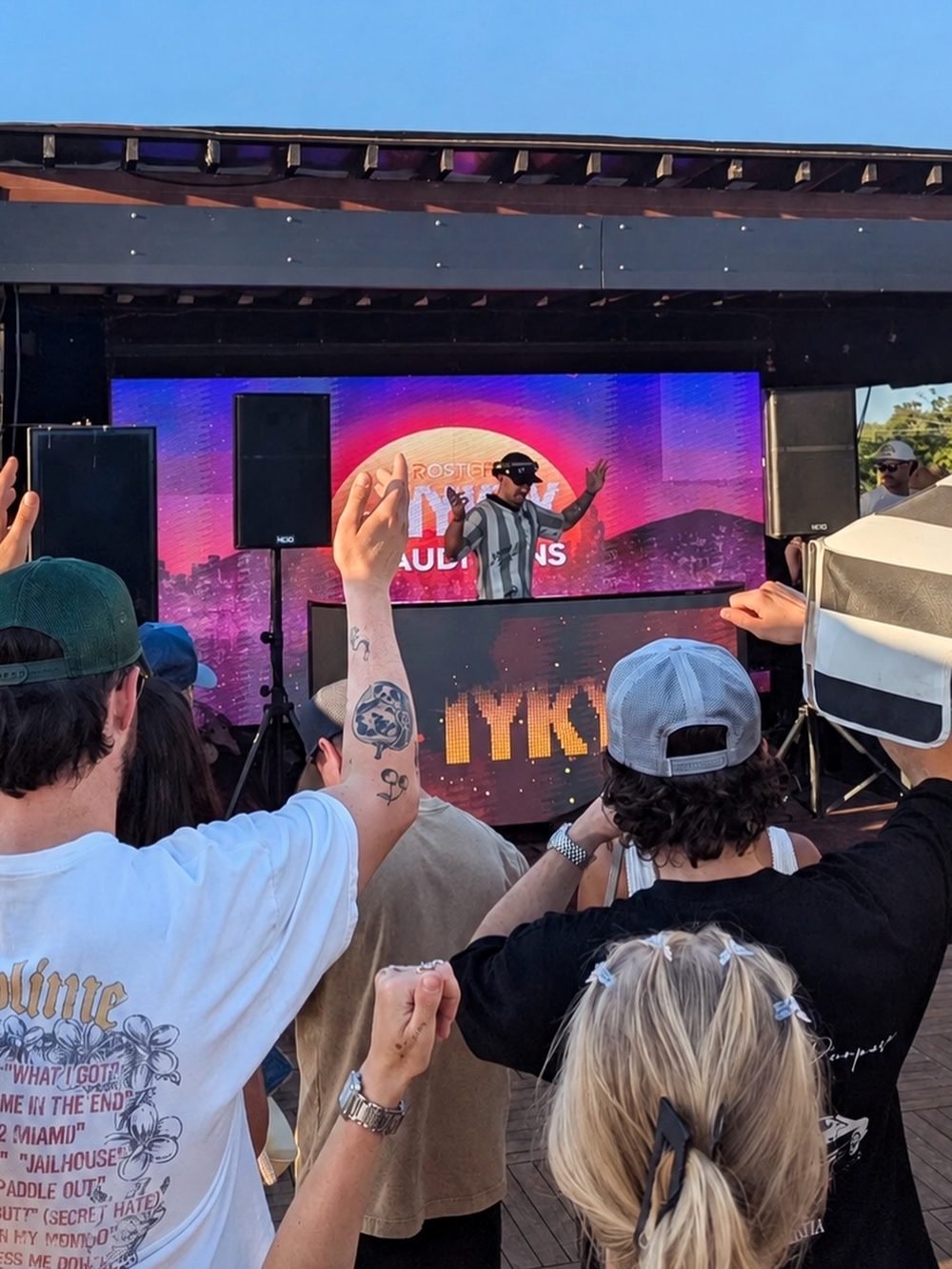 The crowd at the IYKYK live DJ auditions with their hands up, B.Y. on the LED wall behind them.